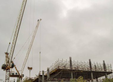 İnşaat vinci ve inşaat halindeki beton yığınları ve demirden yapılmış bir bina bulutlu gri gökyüzüne karşı bir inşaat alanı.