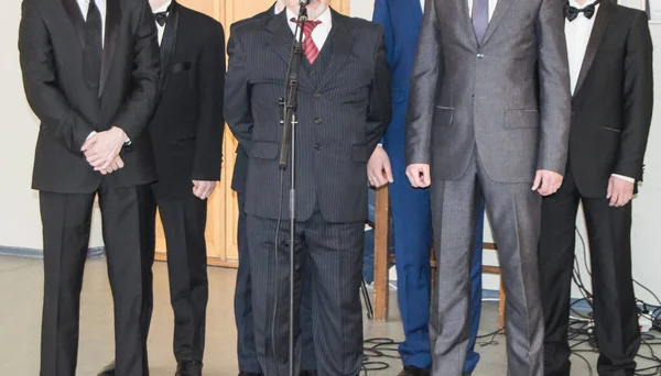 A group of adult Caucasian men in business suits stand at a public performance near a microphone in the performance room — Stock Photo, Image