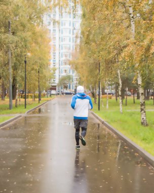 Yağmurlu bir sonbahar gününde genç bir atlet parkta koşar. Spor açık alanda, arkadan..
