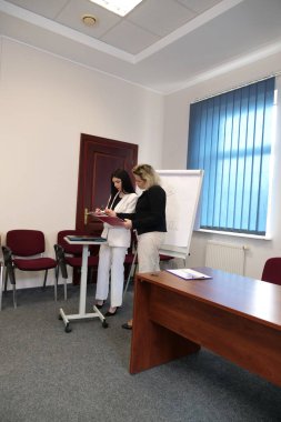 Modern bir ofiste birlikte çalışan iki kadın: bir iş görüşmesi sırasında belgeleri imzalamak ve çizelgeleri bir tabloda tartışmak.