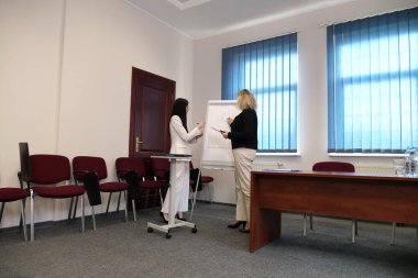 Modern bir ofiste birlikte çalışan iki kadın: bir iş görüşmesi sırasında belgeleri imzalamak ve çizelgeleri bir tabloda tartışmak.