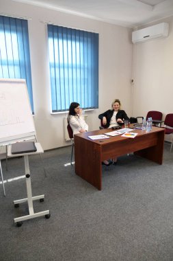 Modern bir ofiste birlikte çalışan iki kadın: bir iş görüşmesi sırasında belgeleri imzalamak ve çizelgeleri bir tabloda tartışmak.