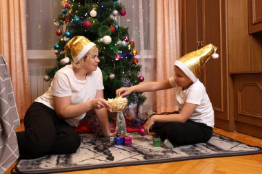 Anne ve oğlu Noel oyuncaklarıyla oynarken patlamış mısır yiyorlar.