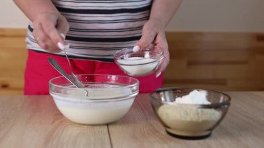 Bir kadın hamuru ekşi krema, yumurta ve un ile hazırlar ve karışımı karıştırır.