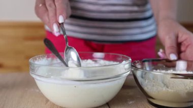 Bir kadın hamuru ekşi krema, yumurta ve un ile hazırlar ve karışımı karıştırır.