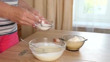 Bir kadın hamuru ekşi krema, yumurta ve un ile hazırlar ve karışımı karıştırır.