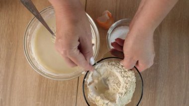 Bir kadın hamuru ekşi krema, yumurta ve un ile hazırlar ve karışımı karıştırır.