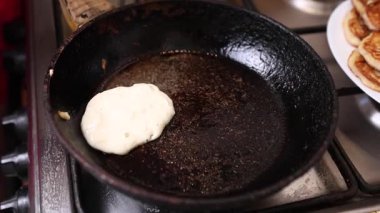 Bir kaşık sıcak tavaya altın kreplerle vururken, bir tabak taze pişmiş börek tutar..