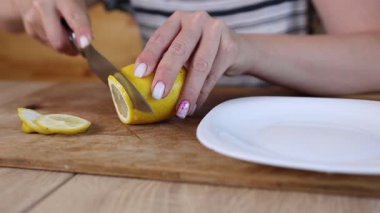 Bir kadın limonu ahşap bir kesme tahtasıyla dilimliyor, turunçgilleri servis için hazırlıyor. Taze limon aromayı ve parlaklığı tabağa ekler..