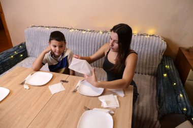 Erkek ve kız kardeş Noel ağacının olduğu bir odaya sofra, tabak, çatal bıçak takımı ve peçeteler kurdular. Ilık ışıklandırma ve yumuşak odaklanma sıcak bir aile ortamı yaratır..