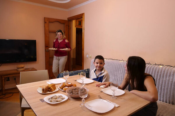Woman brings dishes to festive dinner table with pies, kutia, fish and bread.