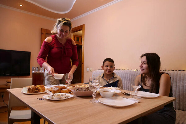 Woman sets food on table, family talks happily in festive atmosphere.