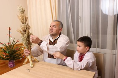 Nakışlı gömlekli bir adam sunar. Buğday sapından yapılmış uzun didük. Geleneksel Ukrayna Noel sembolü..