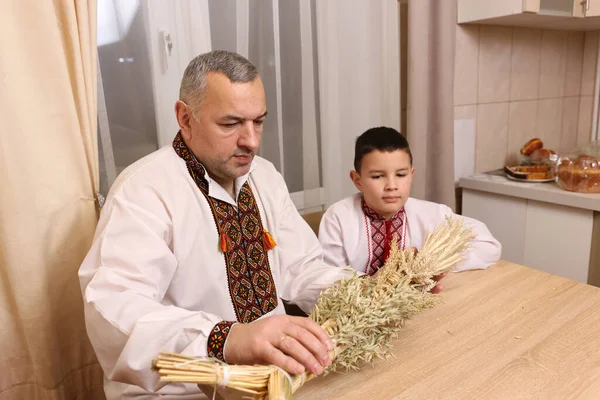 İşlemeli gömlekler içindeki baba ve oğul, zenginliğin sembolü olan buğday saplarından yapılmış didukh 'u inceleyin..