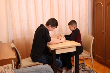 İki çocuk perdeli bir odada masada otururken dikkatle ahşap bir oyun oynuyorlar..