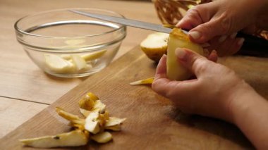 Ahşap tahtada soyulmuş armudu dilimleyen ve cam bir kaseye parçaları yerleştiren kadın..