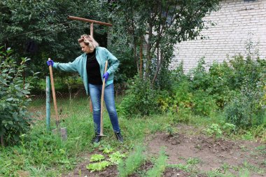 Sebze bahçesinde elinde çapa ve kürekle yataklar üzerinde çalışmaya hazırlanan bir kadın..