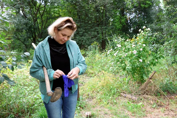 Bahçede işe hazırlanan bir kadın omzunda çapayla koruyucu eldiven takıyor..