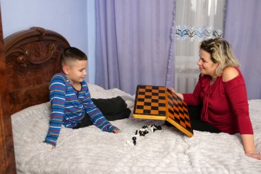 Oğlan ve anne satranç tahtası ve parçaları tutarken gülümserler..