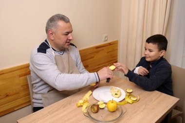 İnsan elmayı masadaki çocuğa uzatır, sıcak bir ilgi ve yakınlık anı yaratır..