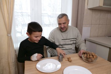 Çocuk fındıkkıranı gülümseyerek ütülüyor, babası da izliyor, masada bir kase ceviz ve tabak..