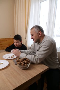 Oğlu ona gülümserken babası ceviz kırıyor. Masaya bir kase ceviz ve kabuk serpiştiriyor..