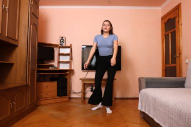 Kadın odaya giriyor, ısınma ve fiziksel aktivite için egzersiz yapıyor.