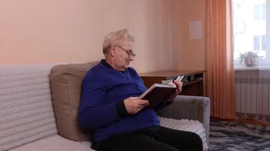 Yaşlı bir kadın kanepeye oturur ve dikkatlice elindeki fotoğraf albümüne bakar..
