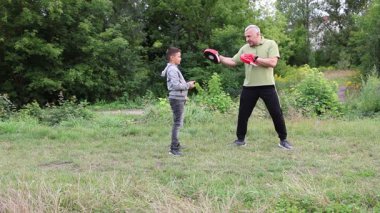 Çocuk, Green Park 'ta yetişkin koçuyla boks antrenmanı yapıyor..