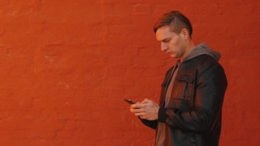 Genç acımasız adam bir smartphone bir turuncu duvar arka planı kullanır. Orta atış