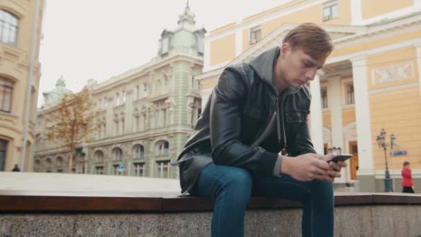 Mladý muž brutální komunikuje v programu messenger v krásném evropském městě. — Stock video