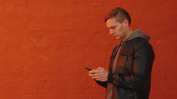 Jovem Homem Brutal Usa Smartphone Contra Fundo Uma Parede Laranja — Vídeo de Stock