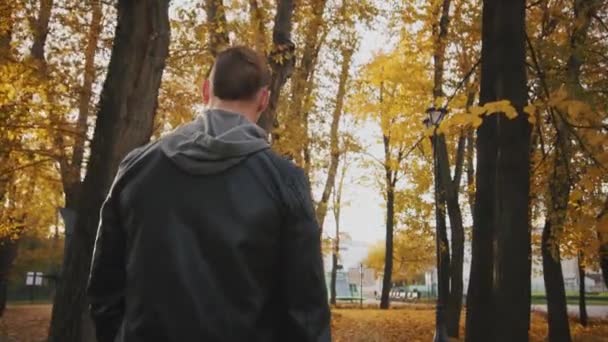 残酷な青年は 黄色の葉で覆われている秋の公園を通ってのトレーニング セッションに行きます 黒い革のジャケットで残忍な男は秋の森を歩く — ストック動画