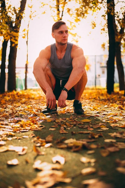 Красавчик, сидящий в осеннем парке в спортивной одежде — стоковое фото