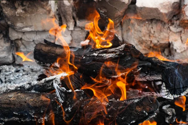 Logs from the fire, which slowly burn out. There is white, light smoke. The logs are black with a white touch of ash. Orange fire is burning. The flame is bright and beautiful.
