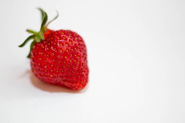 Yeşil kuyruklu güzel bir kırmızı çilek beyaz bir arka plan üzerinde yatıyor. Yalıt