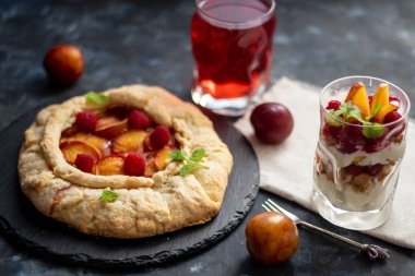 Erikli bisküvi. Fırında pişmiş, ahududu, taze erik, tüm koyu bir arka plan ile süzme peynir krem bir bardak yanında. Gri kumaş ve metal cihazların yakınında. 