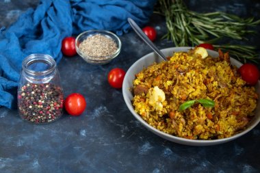 Özbek pilavı yla dolu büyük bir tabak, kiraz domatesin yanında koyu bir bez, elle örülmüş bir standda taze biber. Şeffaf bir tabak, baharat - sıfır ve biber karışımı. Hepsi karanlık bir arka planda.