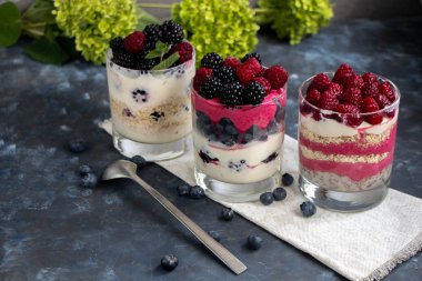 Sağlıklı beslenme Diyet tatlılar. Bardaklar süzme peynir kreması ile doludur, onları chia tohumu, ahududu, yaban mersini, böğürtlen. Arka plan çiçekleri için yakın.