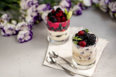 Sağlıklı beslenme Diyet tatlılar. Bardaklar süzme peynir kreması ile doludur, onları chia tohumu, ahududu, yaban mersini, böğürtlen. Arka plan çiçekleri için yakın.