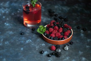 Böğürtlen, yaban mersini, ahududu ile bir tabak yanında, çilek kompostosu ile bir bardak. Tüm bu karanlık bir arka plan üzerinde, çiçeklerle süslenmiş.