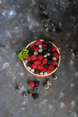 Kahverengi kenarı çilekli bir tabağa koydum. Yaban mersini, ahududu, böğürtlen yan yana, nane yaprakları ile karanlık bir arka plan üzerinde yalan.