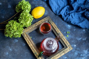 Eski büyükannelerin fotoğraf çerçevesi, elma, bir fincan çay ve eski bir metal şamdan ile bir çaydanlık natürmort. Arkadan, koyu bir arka plan üzerinde mavi kumaş. 