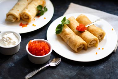 Krep tuzlanmış süzme peynir ile doldurulmuş. Kase ve kaşık kırmızı havyar ve ekşi krema vardır. Nane yaprakları ile dekore edilmiş. 