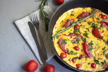 Domates, jambon, biber ve Parmesan peyniri ile Frittata. Gri bir arka plan üzerinde, bir kaşık, kiraz domates ile bir çatal yanında. 