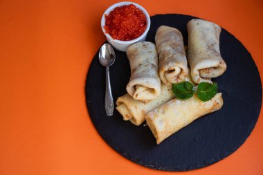 Krep tuzlanmış süzme peynir ile doldurulmuş. Kase ve kaşık kırmızı havyar ve ekşi krema vardır. Nane yaprakları ile dekore edilmiş. 