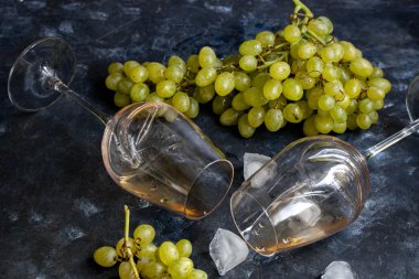 Beyaz üzümler siyah bir tabakta uzanır. Yakınlarda gül şarabıyla dolu iki bardak vardır. Dekorasyon için buz küpleri. Hepsi karanlık bir arka planda.