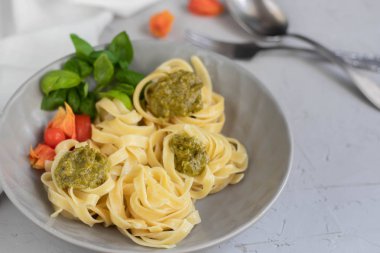 Tagliatelle makarna pesto ile aldente pişmiş. Soslu, physalis, zeytinli kaseye yakın. Eriştefelik yeşil sprigs ile dekore edilmiştir. Sağlıklı yaşam deneyimi. Doğru beslenme. Vejetaryen yemek. 