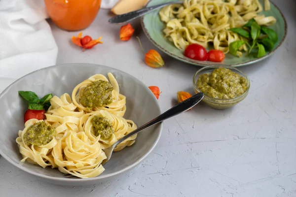 Tagliatelle cooked aldente with pasta pesto. Near bowl with sauces, physalis, olives. The noodles are decorated with green sprigs of basil. Healthy life experience. Proper nutrition. Vegetarian dish.