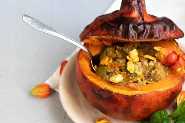 Baked pumpkin stuffed with vegetable stew with rice. Nearby are the berries of physalis, and in the background is a fresh orange tavern. healthy lifestyle. Proper nutrition. Diet.